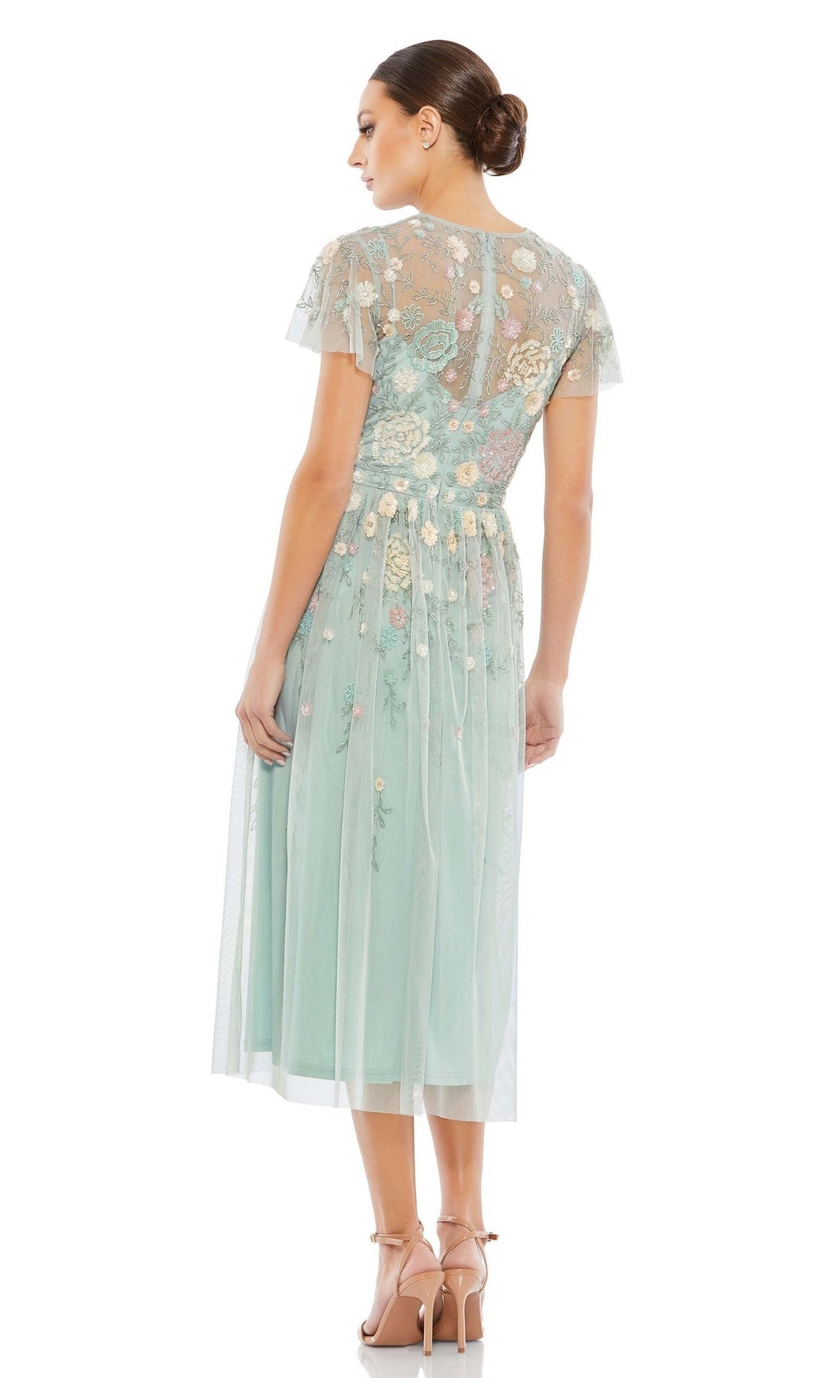 A woman faces away wearing the Mac Duggal Knee Length Wedding Guest Dress 9134, a light blue A-line dress with short sleeves and floral embroidery. She pairs it with nude heels and a low bun. Set against a white background.
